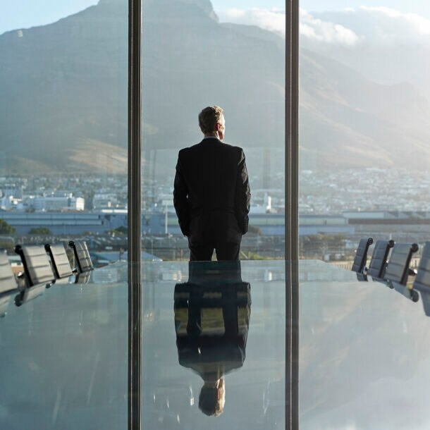 Ein Geschäftsmann blickt aus dem Fenster eines großen Besprechungsraumes auf eine Stadt.