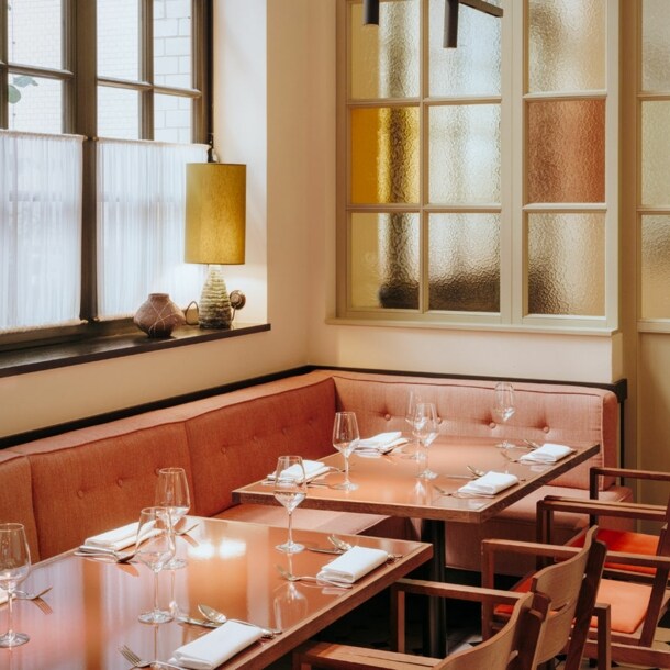 Interieur mit gedeckten Tischen und korallfarbenen Sitzmöbeln am Fenster.
