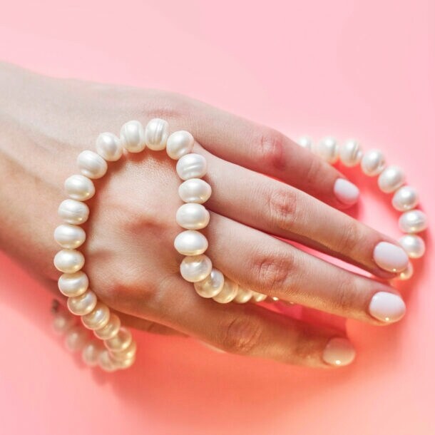 Eine Frauenhand mit Perlenkette umwickelt auf rosa Untergrund