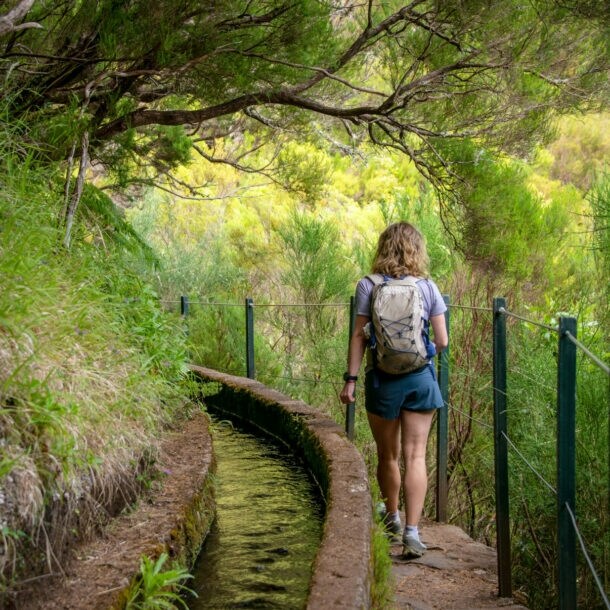 Rückansicht einer Frau auf einem Wanderweg auf Madeira, der entlang eines Bewässerungskanals verläuft.