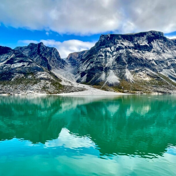Das Bild zeigt dunkle Berge, die aus dem grün schimmernden Wasser des Prins Christian Sunds ragen. 