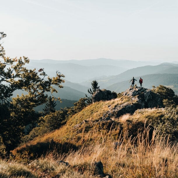 Zwei Personen stehen auf einem Felsen und blicken in die Ferne, im Hintergrund Gipfel im Schwarzwald.