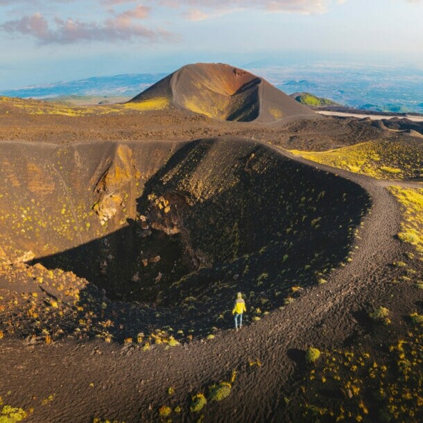 Eine Person steht in einer dunklen Wüstenlandschaft an einem Kraterrand.