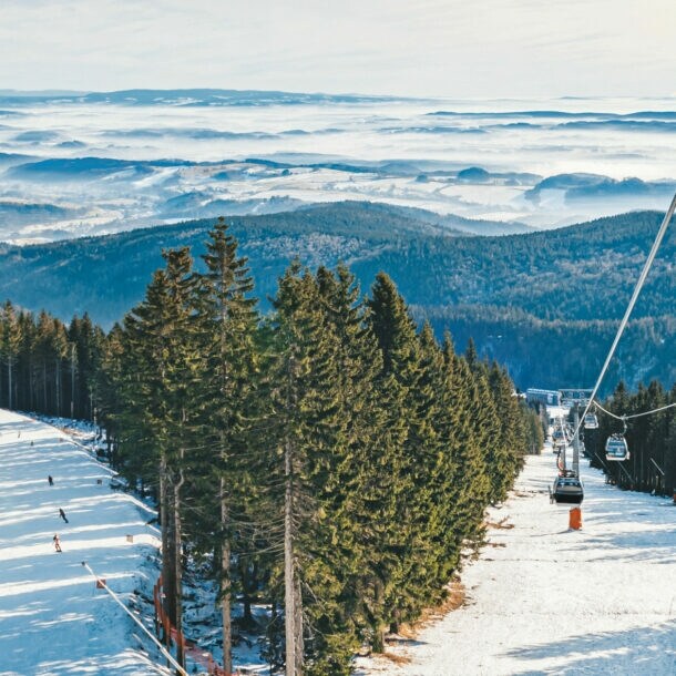 Skilift, der im Riesengebirge über eine Skipiste und Wald verläuft, im Hintergrund Berge.