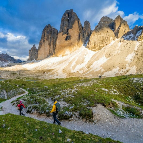 Zwei Personen beim Wandern, im Hintergrund Berge, blauer Himmel und Wolken.