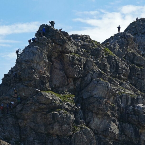 Mehrere Personen, die einen Felsen am Hindelanger Klettersteig erklimmen.