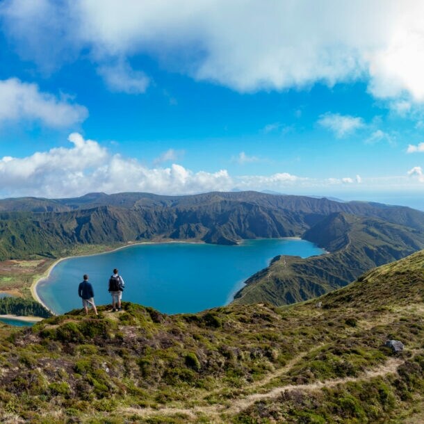 Rückansicht von zwei Personen, die auf einem Hügel stehen mit Blick auf einen See.