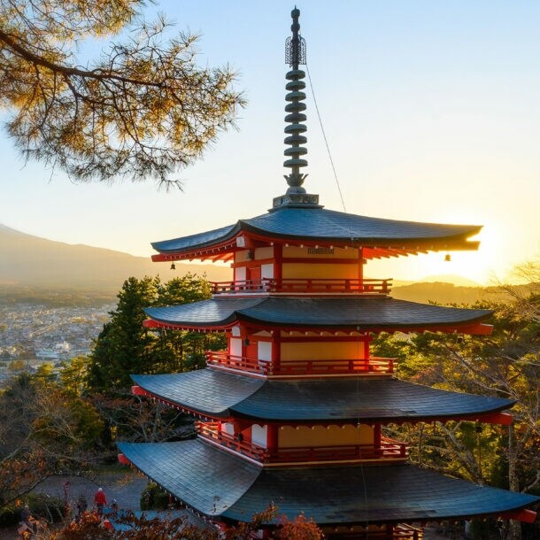 Ein Tempel im Pagodenstil auf einer bewaldeten Anhöhe über einer Stadt, im Hintergrund ein Berg mit Schneekuppe.