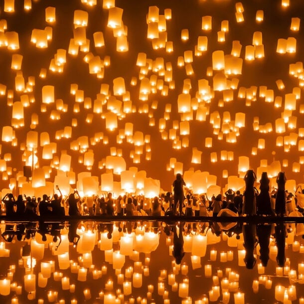 Unkenntliche Personen, die gleichzeitig im Dunkeln unzählige leuchtende Laternen in den Himmel schweben lassen.