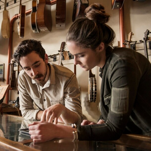 Die Inhaberin und der Inhaber eines Gitarrenshops schauen gemeinsam auf einen Taschenrechner.