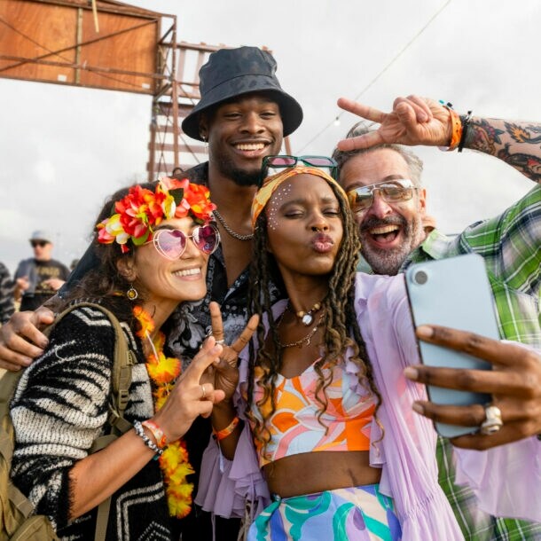 Freunde in bunten Festival-Outfits posieren für ein Selfie.