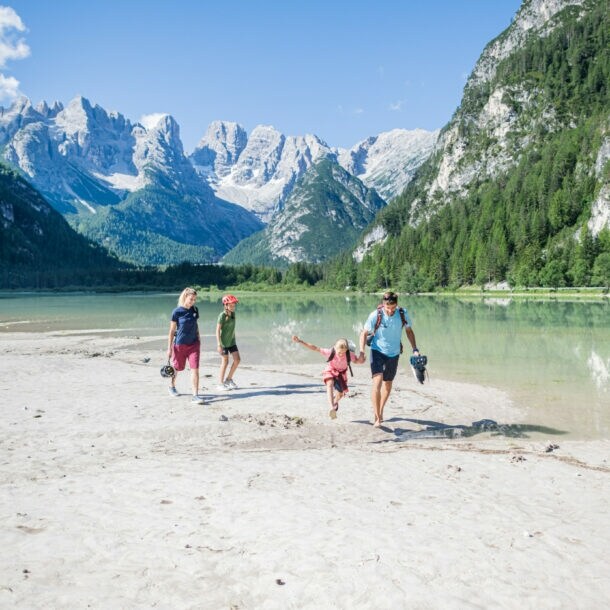 Eine Familie mit zwei Kindern in sommerlicher Sportkleidung läuft an einem See in den Bergen entlang.