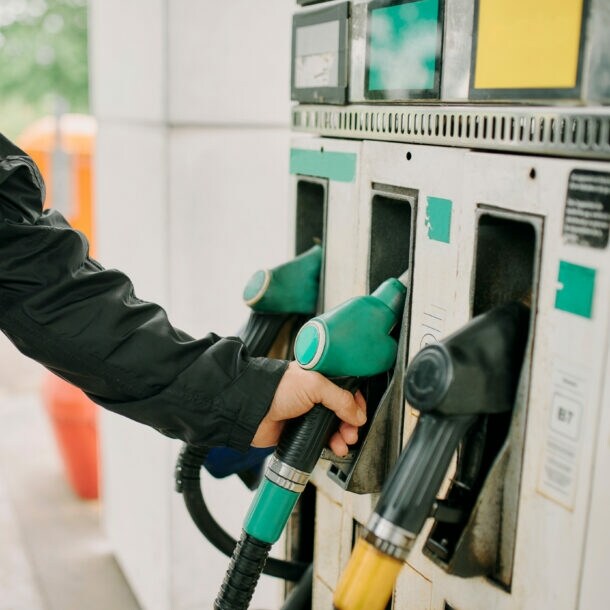 Close-up – Mann greift nach einem Zapfventil an einer Tankstelle.