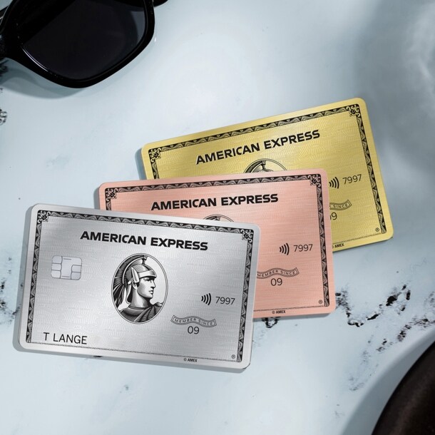 Drei Kreditkarten von American Express liegen auf einem Kaffeetisch aus Marmor, drum herum ist ein Croissants und eine Sonnenbrille.