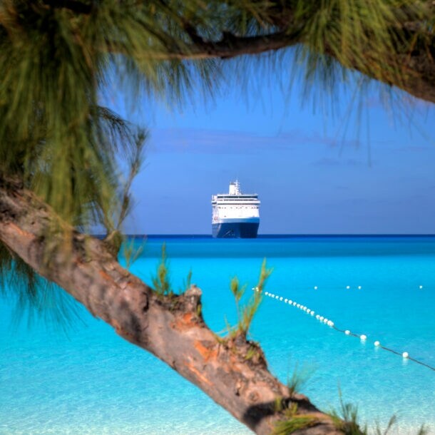 Kreuzfahrtschiff am Horizont eines Karibikstrands mit klarem türkisfarbenem Wasser.