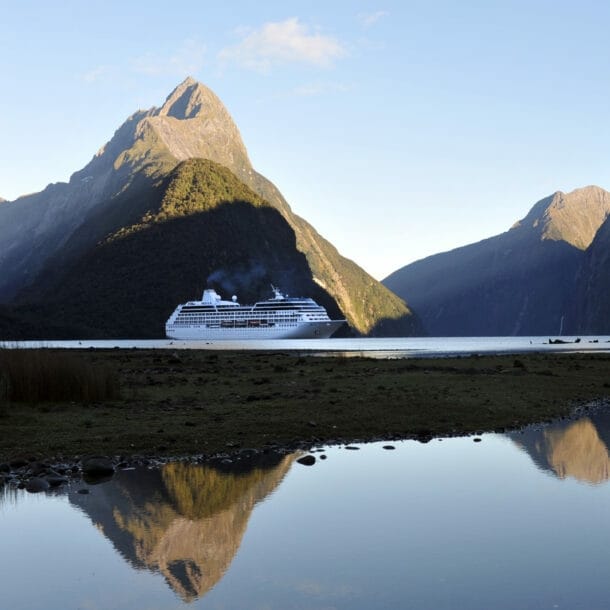 Ein Kreuzfahrtschiff durchquert den Milford Sound in Neuseeland, während sich die hügelige Landschaft des Hintergrunds im ruhigen Wasser spiegelt.