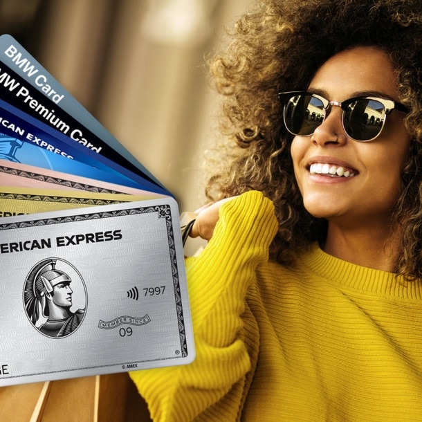 Sieben aufgefächerte Kreditkarten von American Express, im Hintergrund eine lachende Frau mit Sonnenbrille und Einkaufstüten über der Schulter.