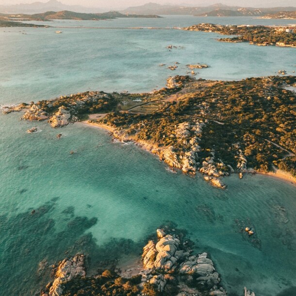 Luftaufnahme einer felsigen Küstenlinie mit klarem, türkisfarbenem Wasser und kleinen Buchten bei Sonnenuntergang.