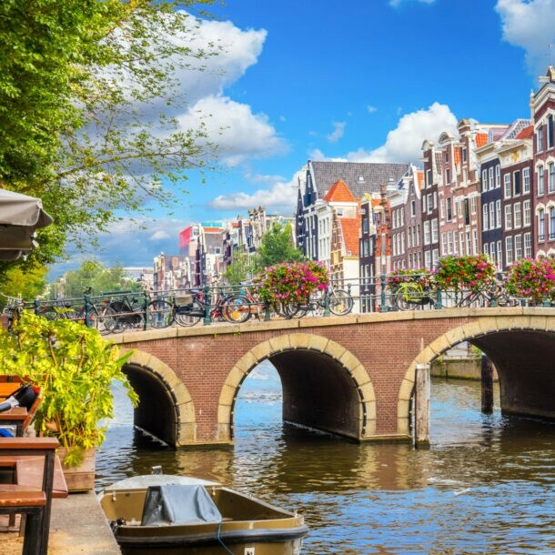 Eine mit Blumen geschmückte Steinbrücke über einem Kanal vor einer Reihe Grachtenhäuser im Stadtzentrum von Amsterdam.