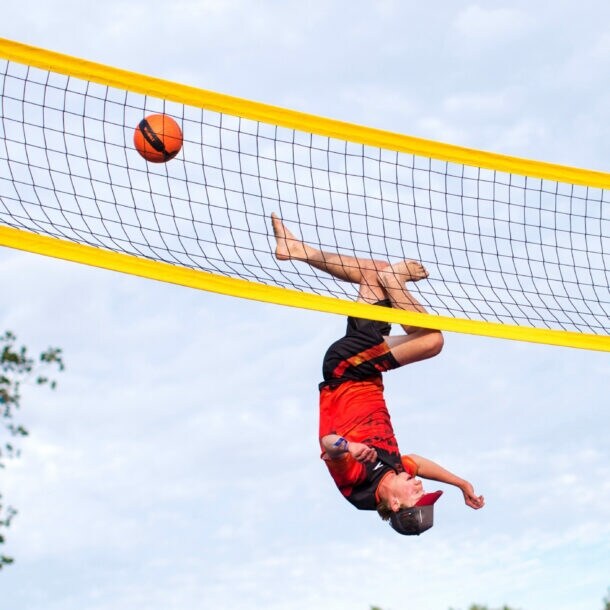 Ein Sportler kopfüber bei einem Sprung an einem Volleyballnetz, daneben ein fliegender Ball.