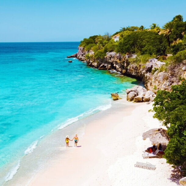Zwei Personen auf einem weißen Sandstrand an türkisblauem Meer in einer Felsbucht mit grüner Vegetation.