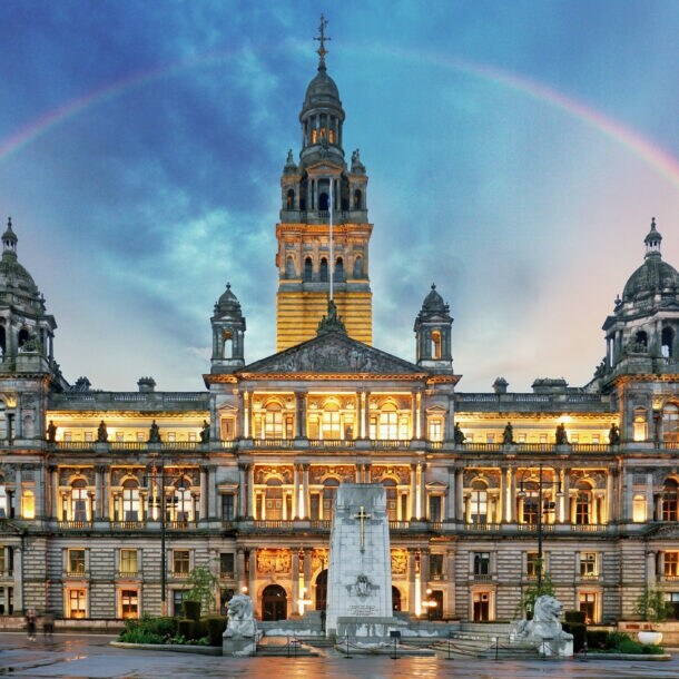 Beleuchtetes historisches Rathausgebäude bei Dämmerung mit Regenbogen am Himmel