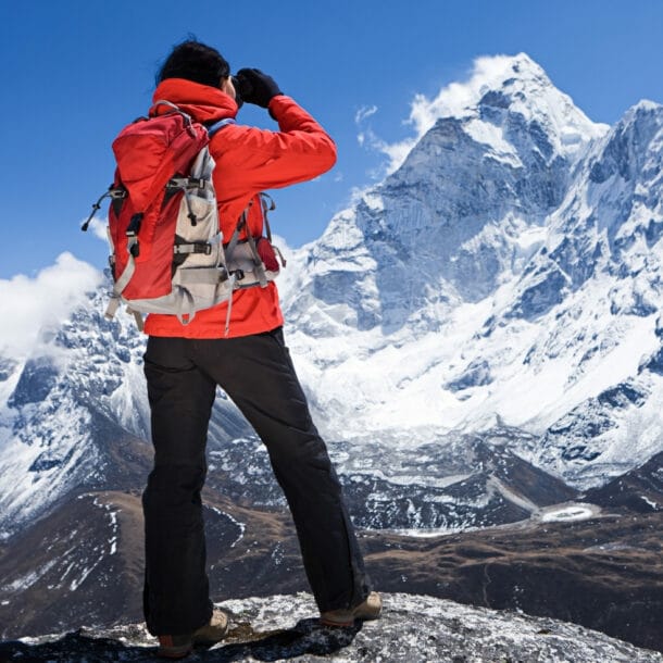 Ein Wanderer in roter Jacke blickt auf einen schneebedeckten Berggipfel im Himalaja