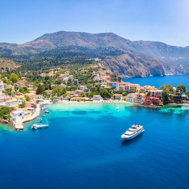 Kleiner Küstenort mit weißen Häusern, umgeben von grünen Hügeln und Bergen, mit klarem blauem Meer und einem Boot im Hafen