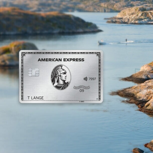 Schärenlandschaft mit Personen im Wasser vor einem roten Holzhaus im schwedischen Stil auf einem Felsen, im Vordergrund eine silberne Kreditkarte von American Express als Freisteller.