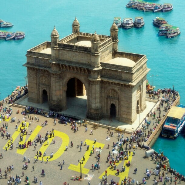 Das Gateway of India, ein großes Tor mit Bögen und Türmen, umgeben von Menschen und Booten im Wasser in Mumbai.