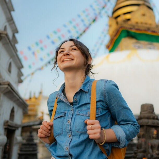 Eine junge, lächelnde Frau mit Rucksack vor einem nepalesischen Tempel.