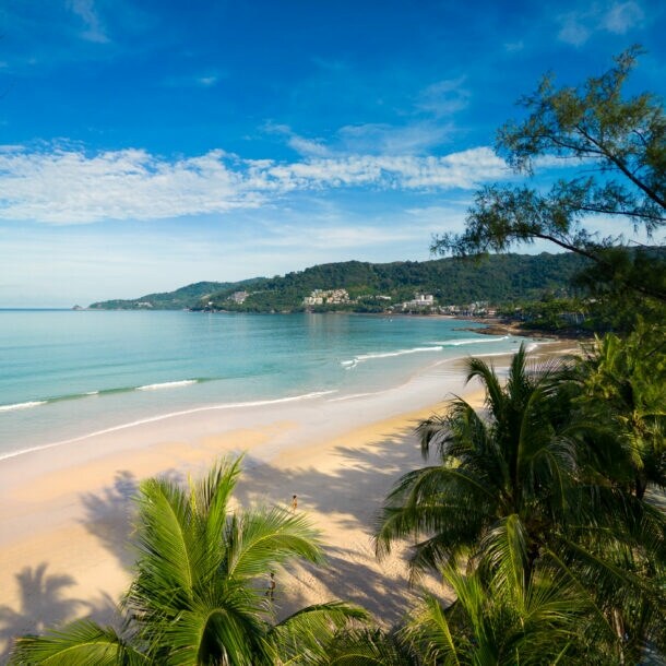 Flache Meeresbucht mit breitem Sandstrand an türkisblauem Wasser, umgeben von tropischer Vegetation.