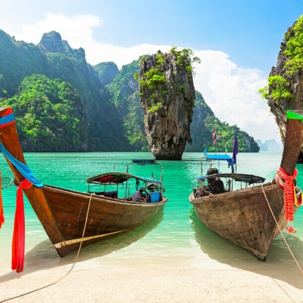 Zwei Holzboote an einem Sandstrand in einer Meeresbucht mit türkisem Wasser, umgeben von begrünten Felsen.