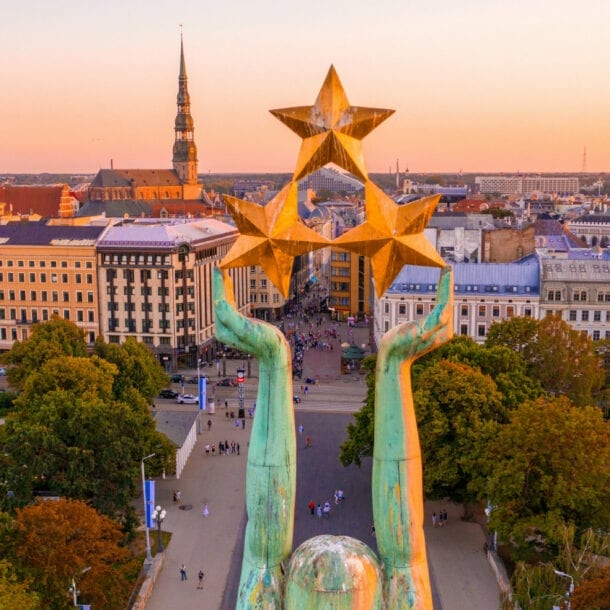 Stadtpanorama von Riga mit Altstadt aus der Luft, im Vordergrund die Arme einer Freiheitsstatue mit drei Sternen.