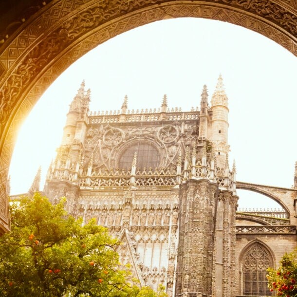 Gotische Kathedrale mit detaillierten Steinmetzarbeiten, gesehen durch einen verzierten Bogenrahmen bei Sonnenlicht