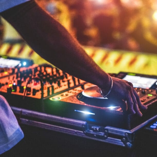 Ein DJ steht vor seinem Mischpult, im Hintergrund ist verschwommen sein Publikum zu sehen.