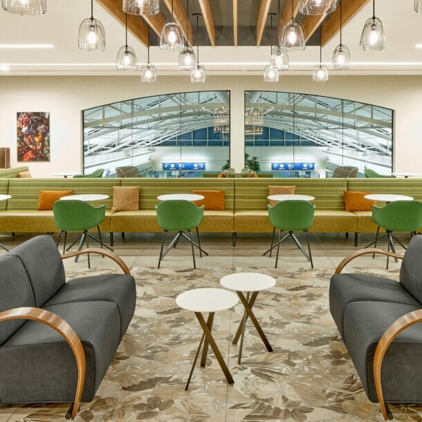 Moderne, elegante Flughafen-Lounge mit unterschiedlichen Sitzgelegenheiten und einem Panoramafenster mit Blick in den Terminal.
