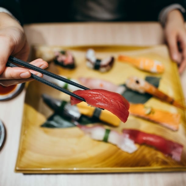 Eine Hand mit Stäbchen über einem Teller mit verschiedenen Sushi-Sorten.