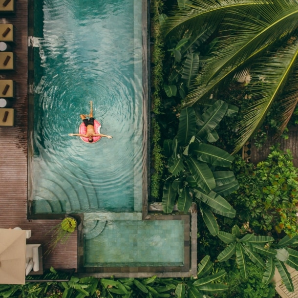 Junger Mann auf einer Luftmatratze in einem Infinity-Pool mit tropischer Umgebung.