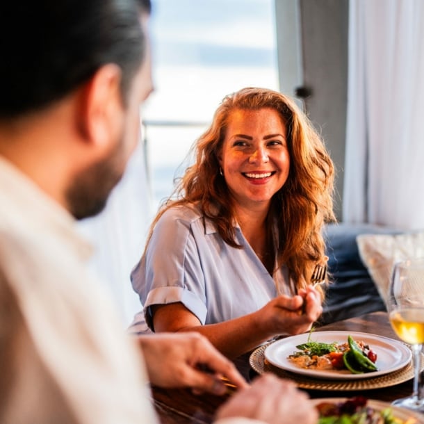 Eine lächelnde Frau im Restaurant sitzt einem Mann gegenüber, zwischen ihnen steht ein hübsch angerichteter Teller.