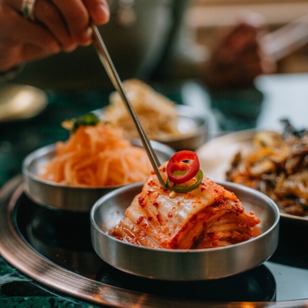 Eine Hand stippt Essstäbchen in eine Schale mit fermentiertem Kohl auf einem Tisch in einem Restaurant.