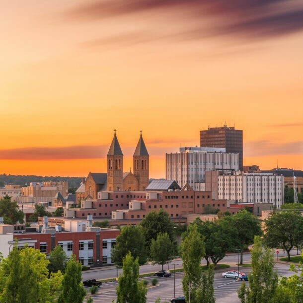 Stadtansicht von Akron bei Sonnenuntergang mit Gebäuden, zwei Kirchtürmen und Bäumen im Vordergrund