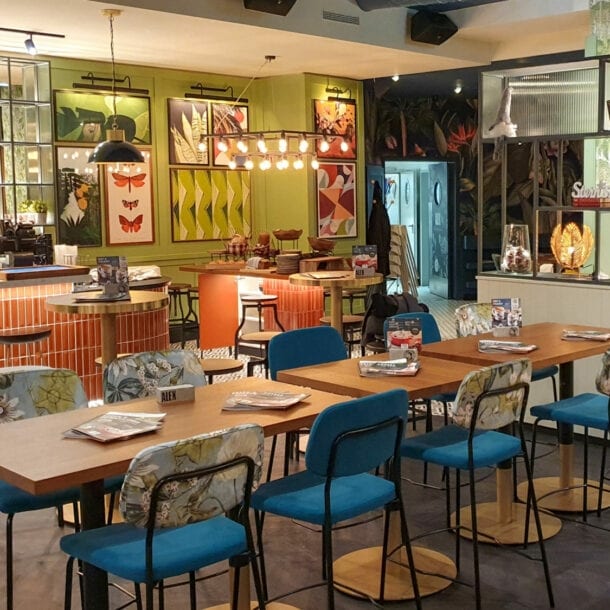 Innenansicht des ALEX in Ludwigshafen, mit Holztischen, bunten Stühlen und dekorativen Bildern an der Wand.