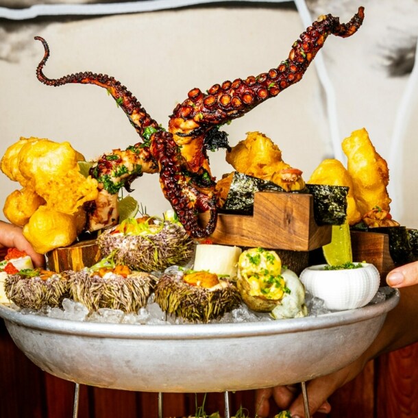 Hände drapieren auf einer tiefen Platte mit Eis diverse Speisen – von Tintenfisch über Frittiertes bis Kaviar.