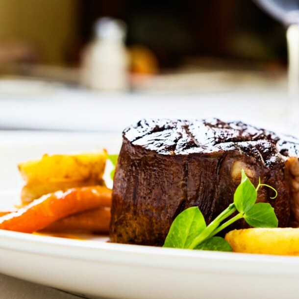 Gegrilltes Rinderfilet auf weißem Teller mit gebratenen Karotten und grünen Erbsensprossen.