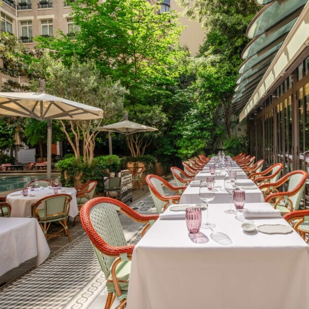 Begrünter Innenhof eines eleganten Restaurants mit gedeckten Tischen und Sonnenschirmen.