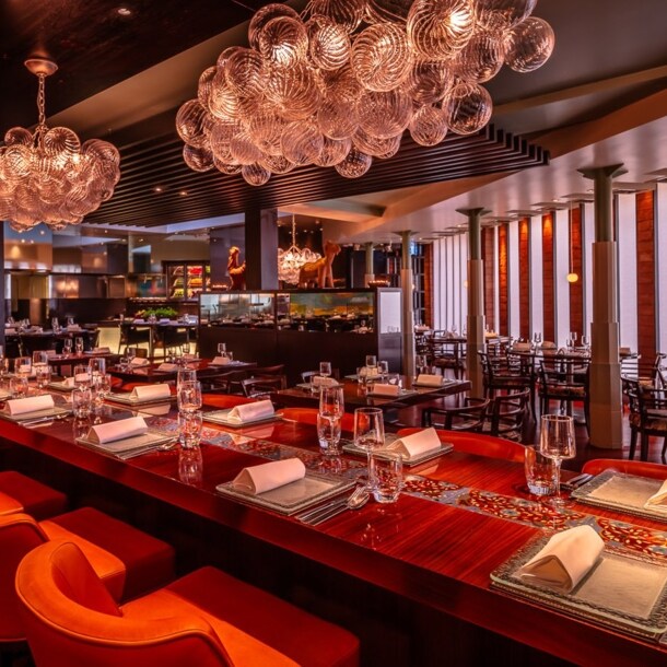 Opulent eingerichteter Speisesaal mit eingedeckter Holztafel und offener Küche.