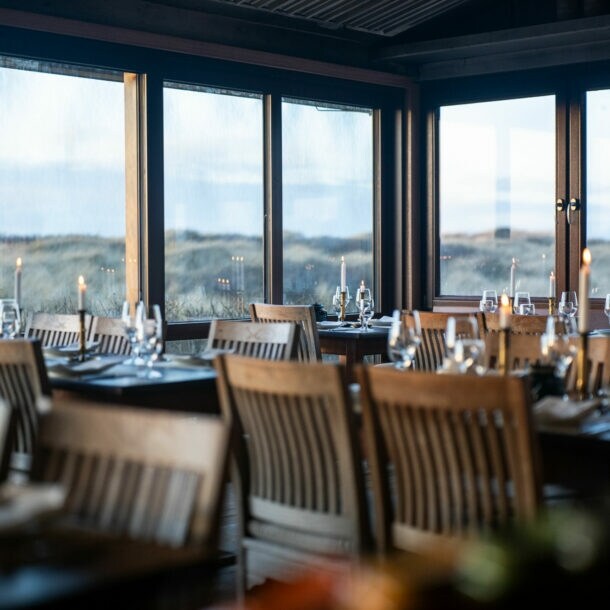 Gastraum der Sylter Sansibar, mit eleganten Tischen und Stühlen aus dunklem Holz und einem herrlichen Ausblick auf die umliegende Dünenlandschaft.