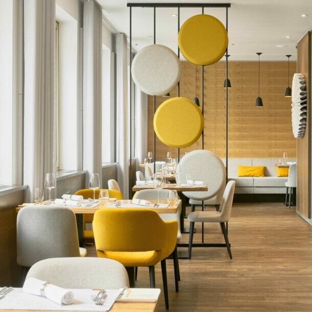 Helles stilvolles Interieur mit gelben und cremefarbenen Sitzmöbeln, dekorativer Trennwand und holzverkleideten Wänden.