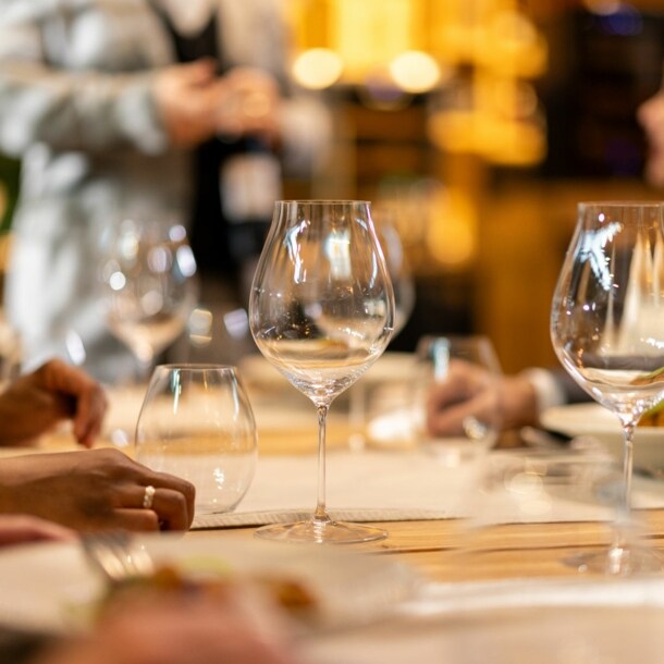 Weingläser auf einem gedeckten Holztisch in einem Restaurant mit Menschen im Hintergrund.